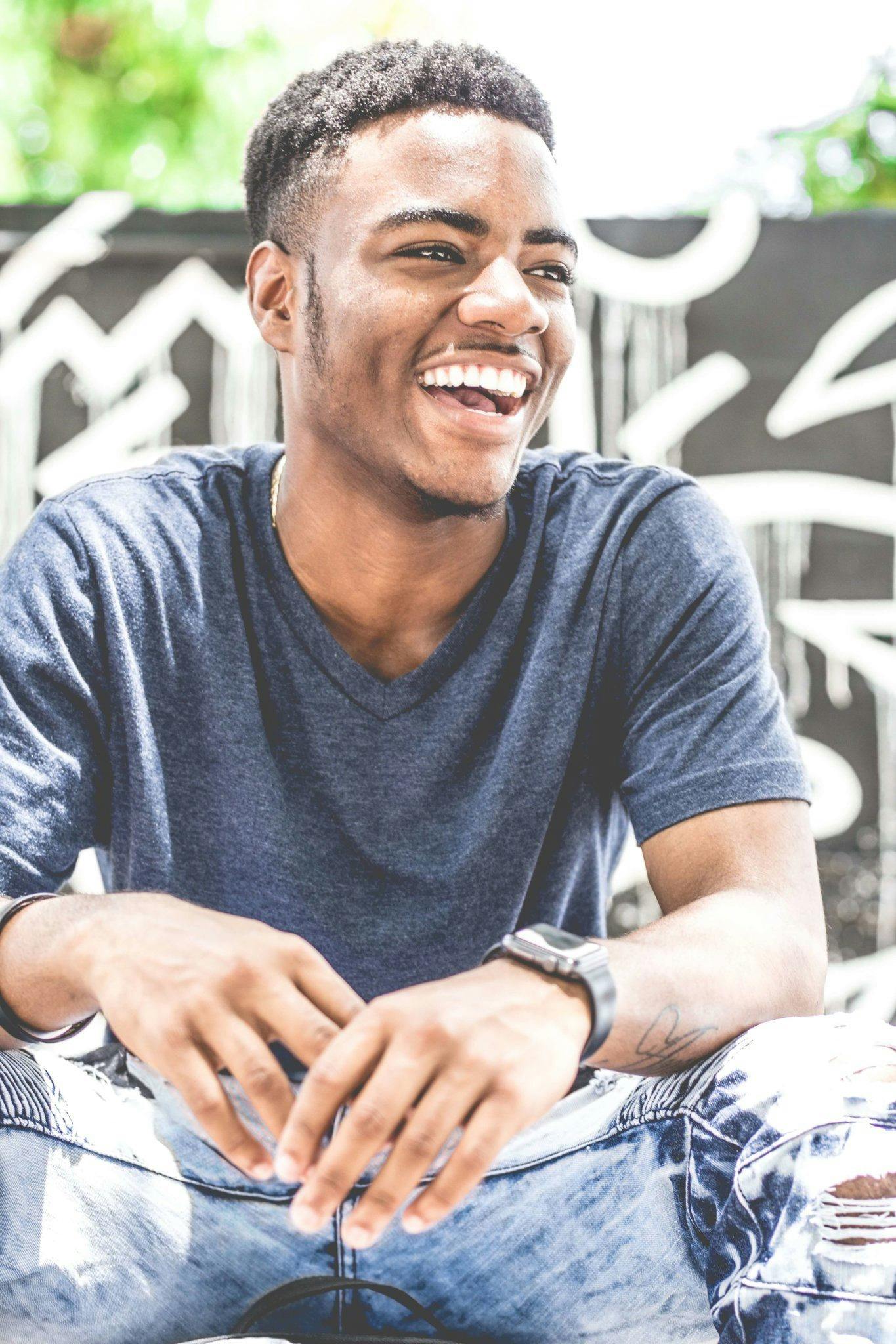 Happy young man sitting outdoors with a bright smile, wearing casual clothing. Ideal for lifestyle and fashion themes.